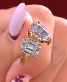 a woman's hand holding a ring with two diamonds on it and a pink manicure