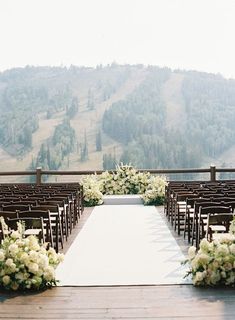 an outdoor ceremony set up with white flowers and greenery on the aisle, overlooking mountains