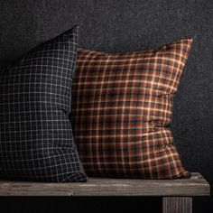 two plaid pillows sitting on top of a wooden table next to a black wall with dark walls