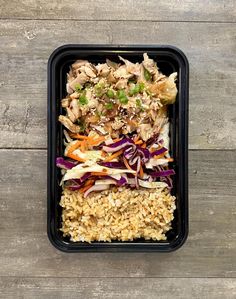 a black container filled with rice, meat and veggies on top of a wooden table