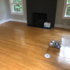 an empty living room with hard wood floors and a fire place in the corner between two windows