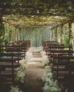 an outdoor wedding ceremony with wooden pews and white flowers on the aisle, surrounded by greenery