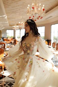 a woman in a white dress with flowers on it and a chandelier hanging from the ceiling