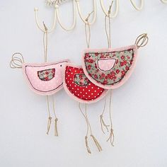 three birds are hanging from hooks on the wall, one is pink and red with white polka dots