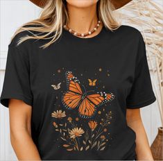 a woman wearing a black t - shirt with an orange butterfly and flowers on it