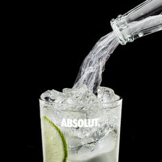 an alcoholic drink being poured into a glass filled with ice and limes on a black background