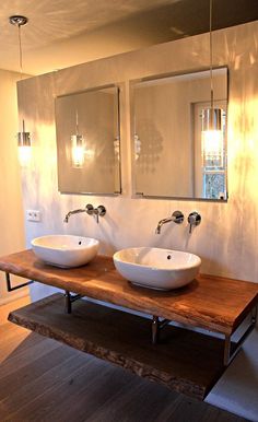 two white sinks sitting on top of a wooden counter in a bathroom next to mirrors