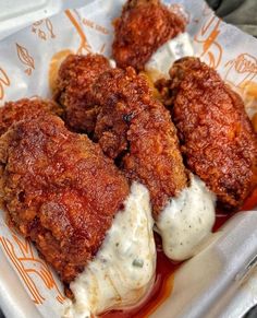 three fried meat patties with sauce and mayonnaise on a paper tray in a takeout container