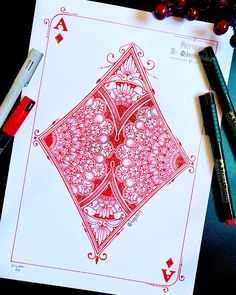 a red and white ace playing card sitting on top of a table next to some pens