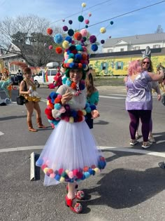 a woman in a colorful dress and hat with pom - poms on her head