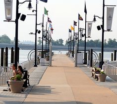 two people sitting on a bench next to the water with flags flying in the background