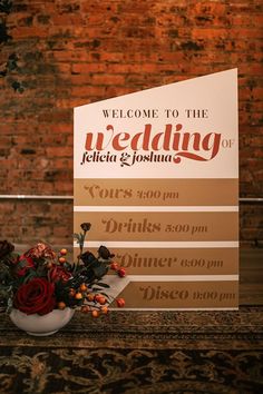 a welcome sign with flowers in a vase on a table next to a brick wall