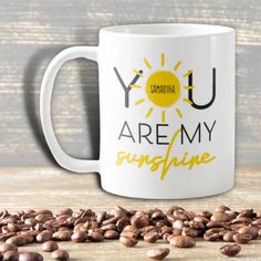 a coffee mug with the words you are my sunshine printed on it next to roasted coffee beans