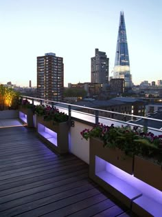 an outdoor deck with planters and lights in the city at sunset or dusk, overlooking london's skyscrapers