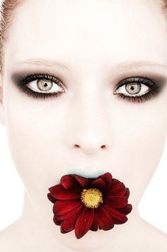 a woman with dark makeup has a flower in her mouth