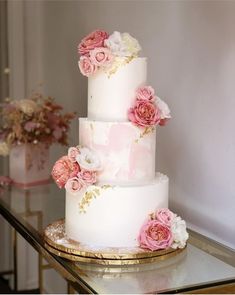 a three tiered cake with pink and white flowers on the top is sitting on a table