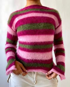 a woman wearing a pink and green striped sweater standing in front of a white wall