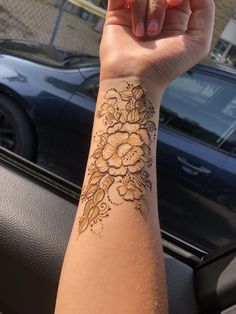 a woman's arm with a flower tattoo on it, in front of a car