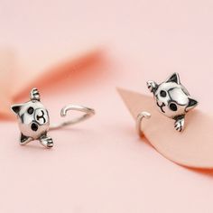 two silver cat earrings sitting on top of a pink surface