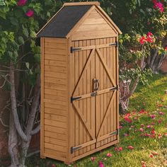 a wooden storage shed in the garden with pink flowers around it and a fence behind it