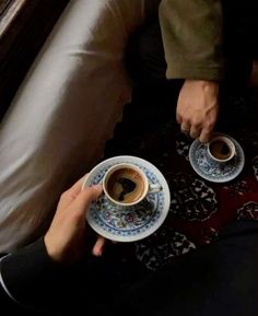 two people sitting on a couch holding cups of coffee and saucers in their hands