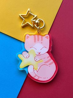 a keychain with a cat holding a star on it's back, sitting on top of a multi - colored background