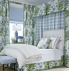 a bedroom with blue and green floral wallpaper, white bedding, and curtains