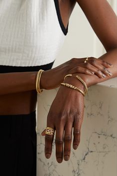 two women wearing gold bracelets and rings on their hands, one is holding the other's hand