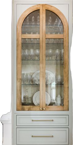 a china cabinet with glass doors and wooden trim around the top, in front of a white wall