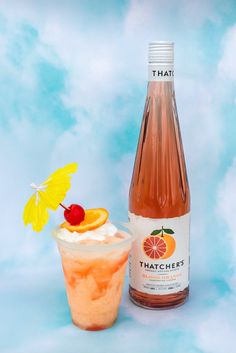 a bottle of peachade next to a glass with an orange garnish on it