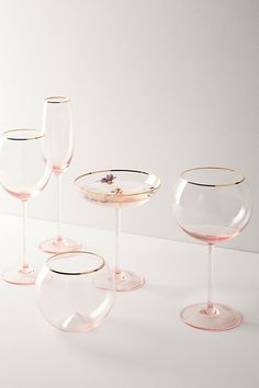 three wine glasses sitting next to each other on top of a white table with gold rims