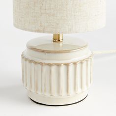 a white ceramic lamp with a gold trim around the base and a beige fabric shade