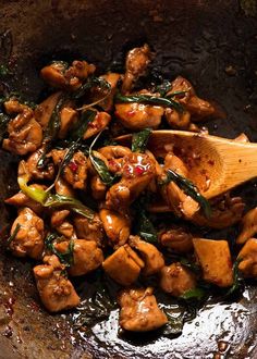 chicken and spinach stir fry in a wok with a wooden spoon on the side