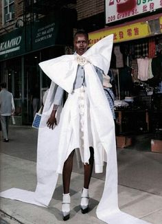 a woman is standing on the sidewalk wearing a dress made out of white cloths