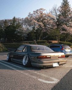 two cars parked in a parking lot with trees in the back ground and one car behind it