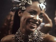 a woman with lots of hair and jewelry on her head smiles at the camera while another person holds up their hand