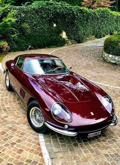 a red sports car parked in front of some bushes and shrubbery on a brick driveway