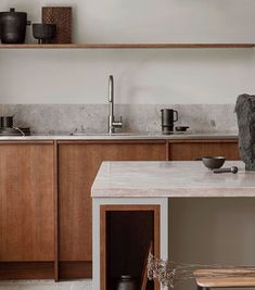 a modern kitchen with wooden cabinets and white counter tops, black vases on the shelf