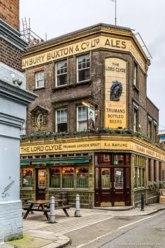 an old brick building on the corner of a city street with tables and benches in front of it