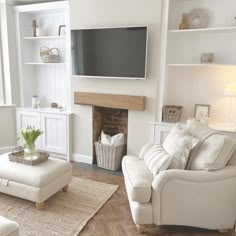 a living room with white furniture and a flat screen tv mounted on the wall above a fireplace