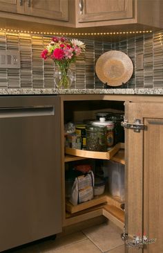 an open cabinet in a kitchen with flowers and other items on the counter top next to it