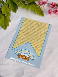 an open book sitting on top of a table next to some pink flowers and green leaves