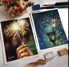 two paintings of fireworks being held by someone's hand and on the table next to them is a vase with flowers