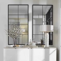 two mirrors are on the wall above a white cabinet and vase with flowers in it