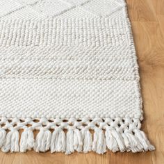 a white rug with tassels on top of a wooden floor next to a wood floor