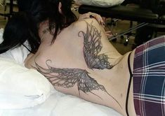 a woman laying in bed with a tattoo on her back and wings above her stomach