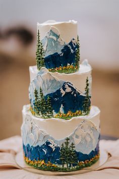 a three tiered cake decorated with mountains and trees