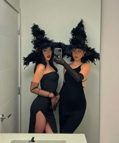 two women in black dresses taking a selfie in a bathroom mirror with one holding a cell phone