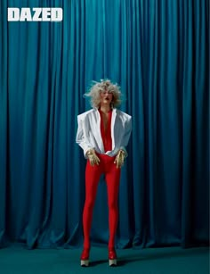 a woman in red pants and white shirt posing for a photo with blue curtains behind her