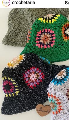 three crocheted hats sitting next to each other on a white surface with a tag